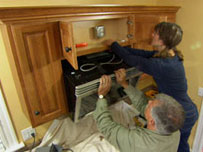 tom silva helps a homeowner install a combination range hood and microwave oven over her kitchen stovetop