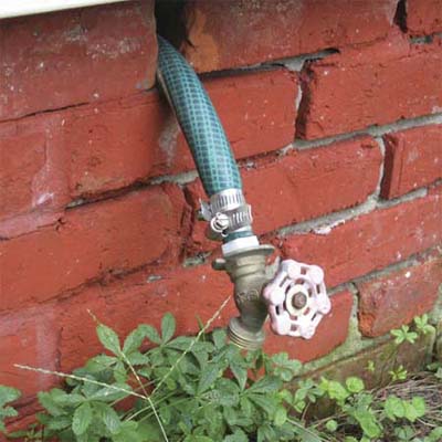 hose connector hanging off a length of garden hose stuck through an open hole in an exterior wall