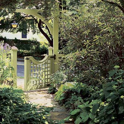 Garden with an arch entry and paved walkway has a hanging lampost