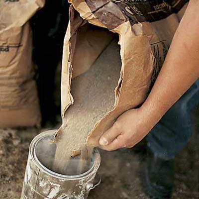 man pouring sand from a bag into a barrel