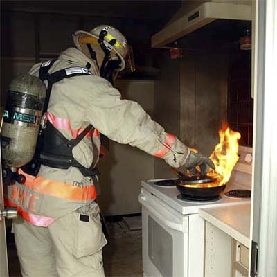 fireman putting out a flaming fry pan in a kitchen