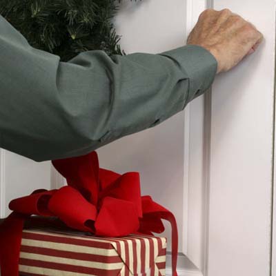 one hand knocking on decorated front door of a house while the other holds a wrapped gift