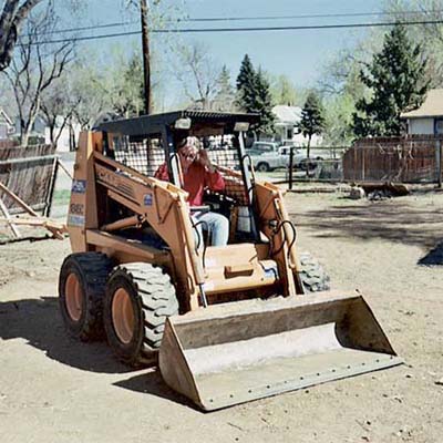 homeowner driving her rented skid-steer in the yard during her remodel