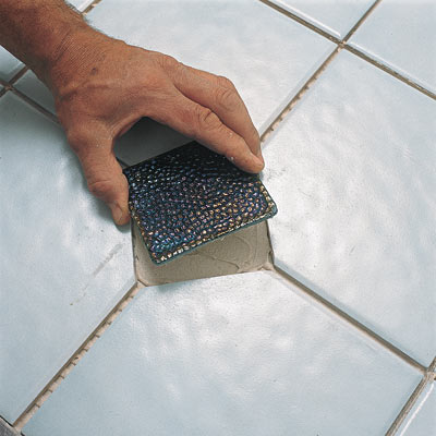 hand placing ceramic tile on bathroom floor