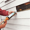 man caulking house exterior for replacement clapboard