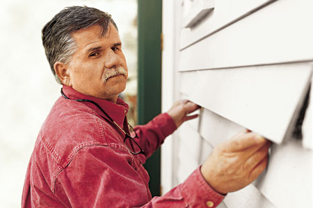 man replacing damaged clapboard with new one