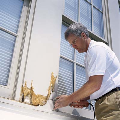 man repairing damaged wood on exterior of house