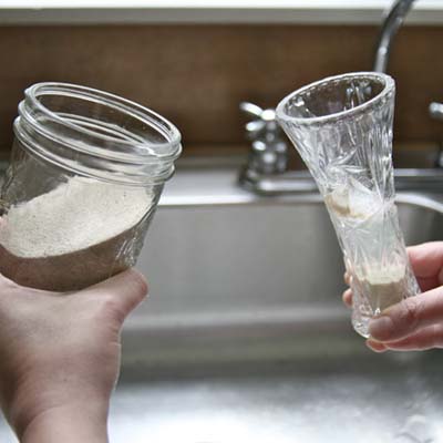 person using sand to clean narrow necked glass container