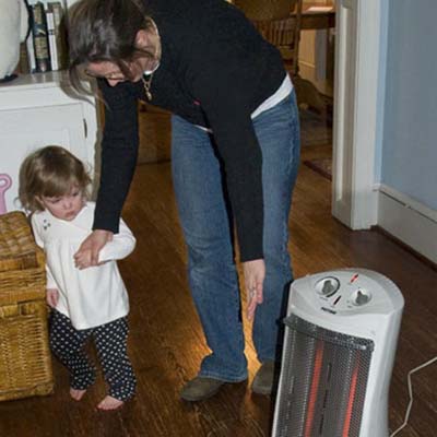 child home safety, child-proofing, and accidental injury prevention in the living room: woman guiding girl away from space heater