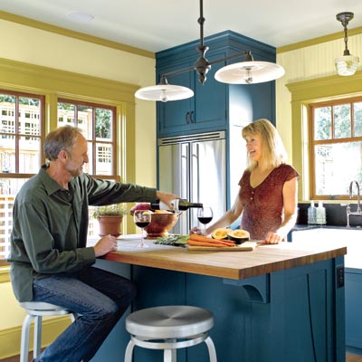 couple entertaining in kitchen with blue cabinets and olive walls