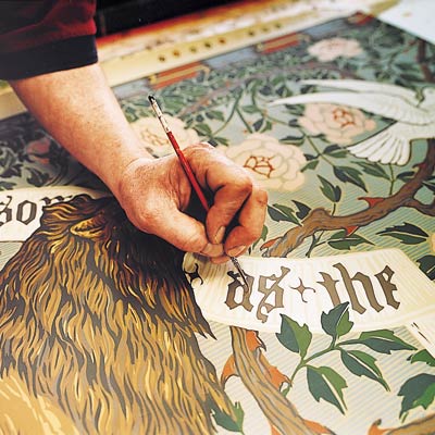 Arts and Crafts-style Lion and Dove frieze wallpaper being touched up by hand