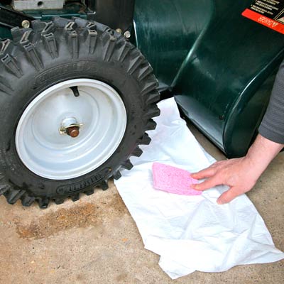 hand putting sponge under lawn mower to catch oil leak