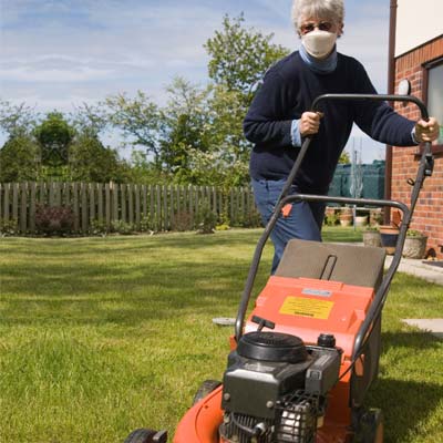 woman with a mask mowing the lawn