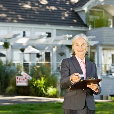 real estate broker handing out business card in front of house