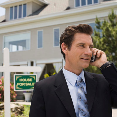 real estate broker talking on cell phone in front of house for sale