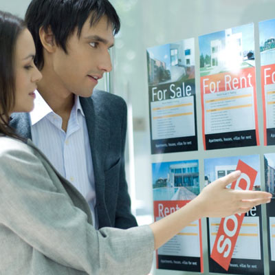 man and woman looking at window of large real estate agency