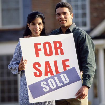 couple holding sold house sign on front lawn
