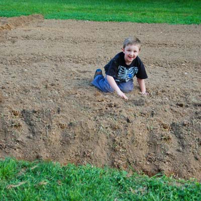 little boy sitting on patch of dirt in yard