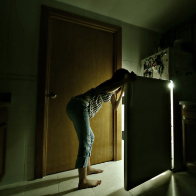 woman looking in fridge for snack in a dark kitchen