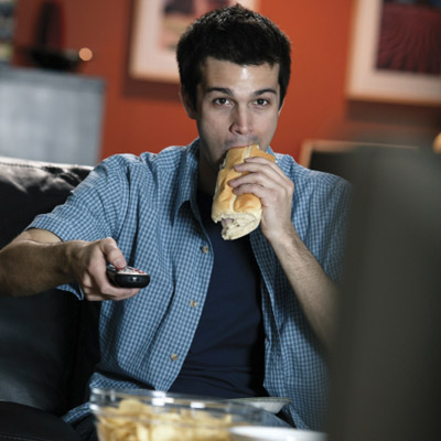 man eating a sandwich while he watches TV