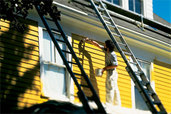 person on scaffold painting exterior of house yellow