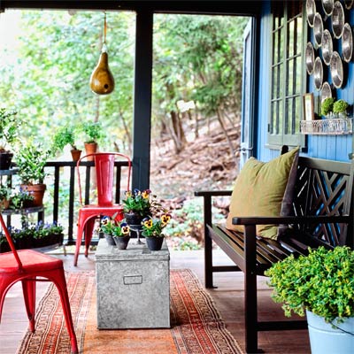 a porch with pie-tins on the wall, a bench, red metal chairs and a gourd birdhouse
