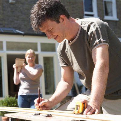 man cutting piece of wood in yard with woman 