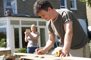 man cutting wood in front yard with woman