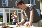 man cutting wood in front yard with woman