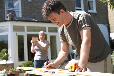 man cutting wood in front yard with woman