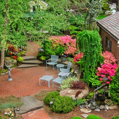 yard with brick gathering spots surrounded by stone walls, conifers and azaleas