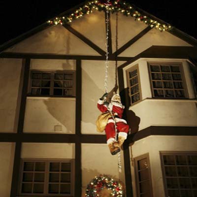 A figure of Santa scaling the side of a Tudor-style home