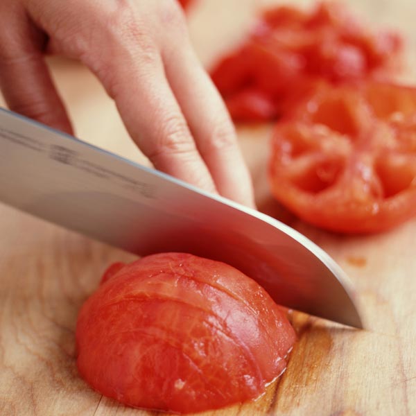 person slicing tomato with sharp knife