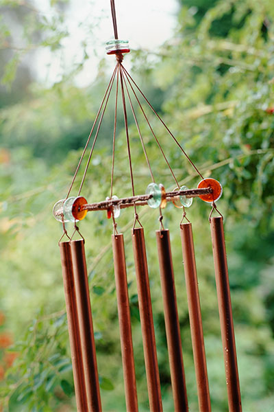 copper pipe wind chime hanging in a yard with blurry trees in the background