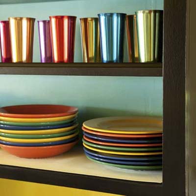 close up of painted open shelves displaying colorful plates and metal glasses