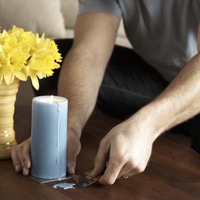 gift card being used to scrape candle wax from a wooden table