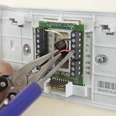 connecting wires to a new thermostat using needlenose pliers and a screwdriver