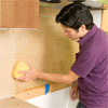 man applying water from a sponge to the paper-covered tile sheets of a glass mosaic backsplash
