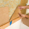 man peeling the paper-covering from the installed tile sheets of a glass mosaic backsplash