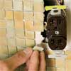 man installing individual tiles to fit around obstructions in a glass mosaic backsplash
