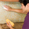 man cleaning the tiles to grout the installed glass mosaic backsplash