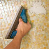 man grouting the joints of the installed glass mosaic backsplash