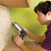 man caulking the perimeter of the installed glass mosaic backsplash