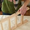 hands using a drill to attach the spindles and legs for building a dog gate