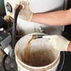 latex-gloved hands hold a hose attached to a water heater that is draining sediment-tinged water