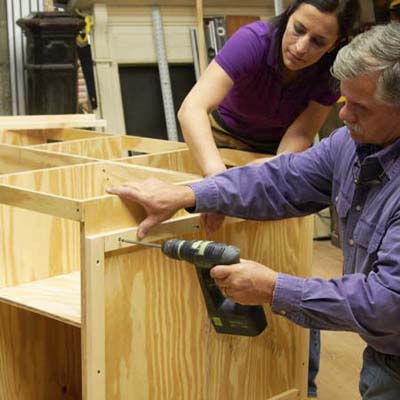 Tom Silva and Amy Paladino install furring strips in order to mount the pegboard on the side of the tool bench