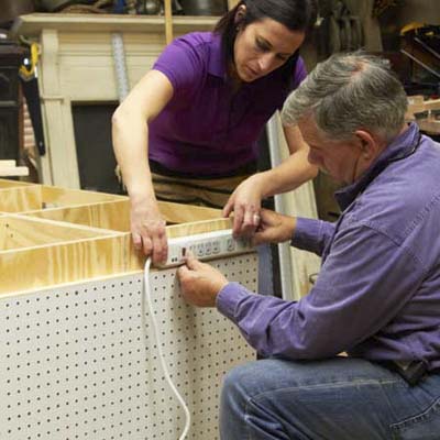 Tom Silva and Amy Paladino mount a power strip to the side of the tool bench