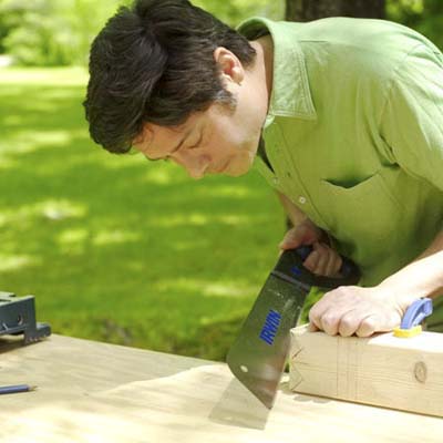 man using pull saw to make king crown for yard game of kubb
