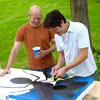 two men removing tape of design for cornhole game board