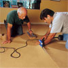 two people using an electric seaming iron to demonstrate how-to install carpet